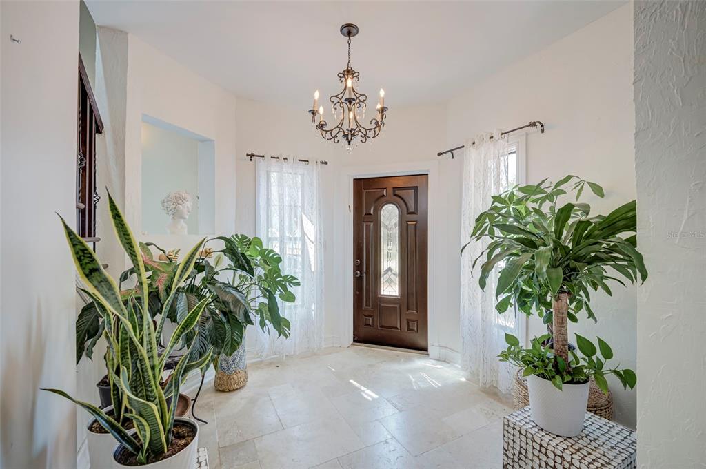A bright entryway features a dark wood front door, a chandelier, and several potted plants — 2491 PALM TREE DRIVE, PUNTA GORDA, FL