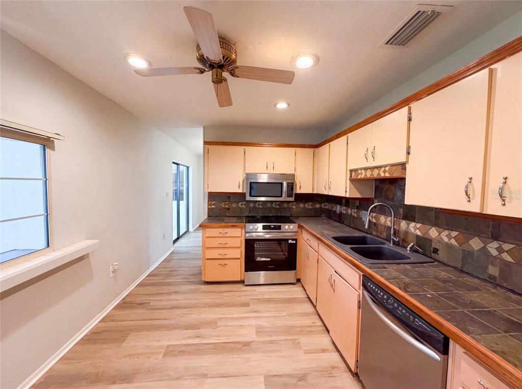 A kitchen features light-colored cabinets, dark tile countertops, stainless steel appliances, and wood-look flooring — 466 LELAND DRIVE, DELTONA, FL