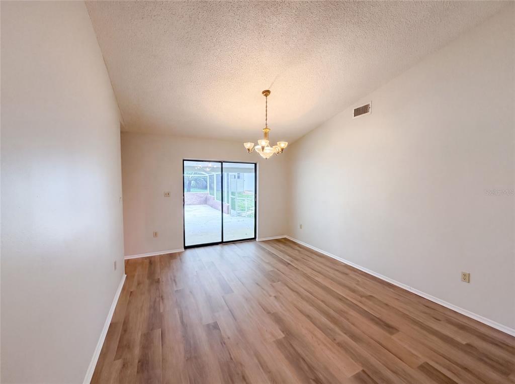 An empty dining room features wood-look flooring, a chandelier, and sliding glass doors to a patio — 466 LELAND DRIVE, DELTONA, FL