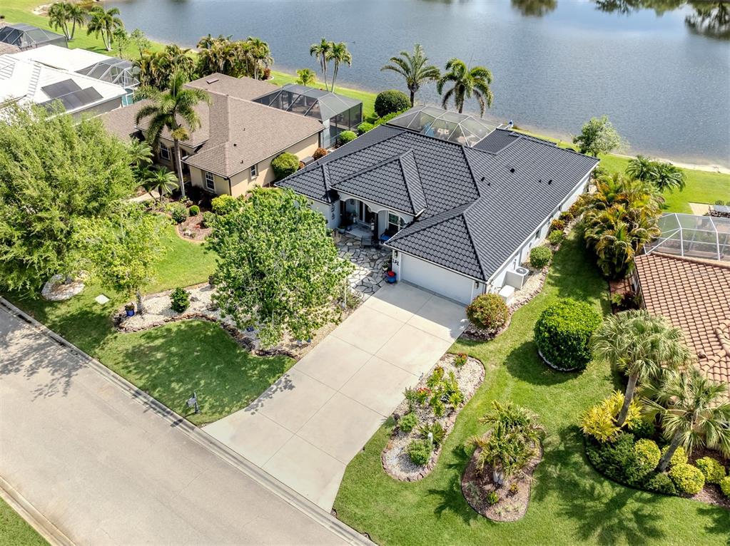 An aerial view shows a single-story house with a dark roof and a lakefront backyard — 132 WADING BIRD DRIVE, VENICE, FL