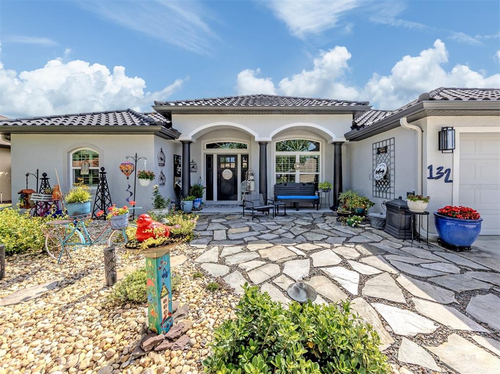 A single-story house with a stone patio, arched entryway, and decorative garden accents — 132 WADING BIRD DRIVE, VENICE, FL