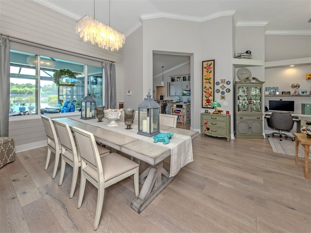 A dining room with a long wooden table, upholstered chairs, and a view of a patio — 132 WADING BIRD DRIVE, VENICE, FL