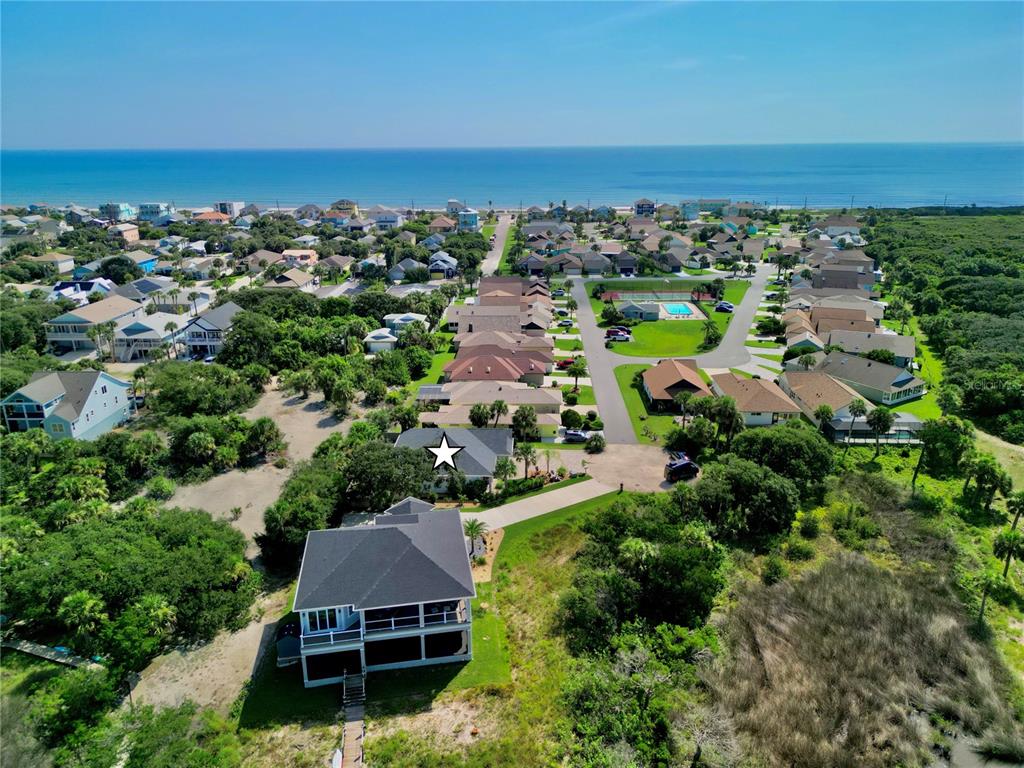 An aerial view shows a coastal neighborhood with houses, a swimming pool, and the ocean — 63 BEACHWOOD DRIVE, FLAGLER BEACH, FL