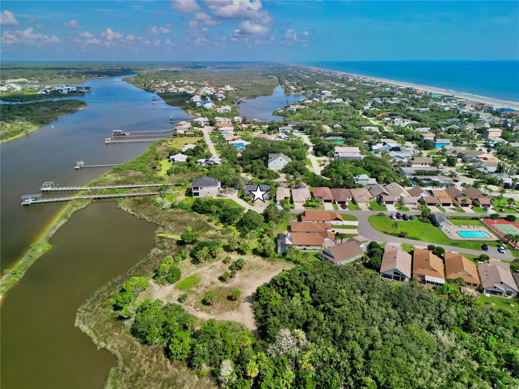 An aerial view shows a coastal neighborhood with houses, a waterway, and a beach — 63 BEACHWOOD DRIVE, FLAGLER BEACH, FL