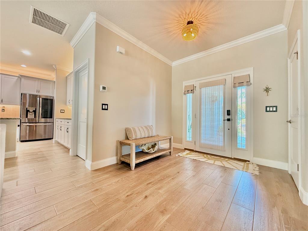An entryway with light wood-look tile flooring, a wooden bench, and a glass-paneled front door — 63 BEACHWOOD DRIVE, FLAGLER BEACH, FL
