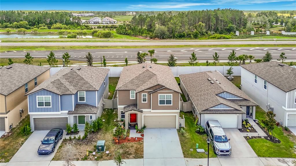 An aerial view shows three suburban houses with driveways and garages facing a multi-lane road — 35186 ACKLEY TRACE, ZEPHYRHILLS, FL