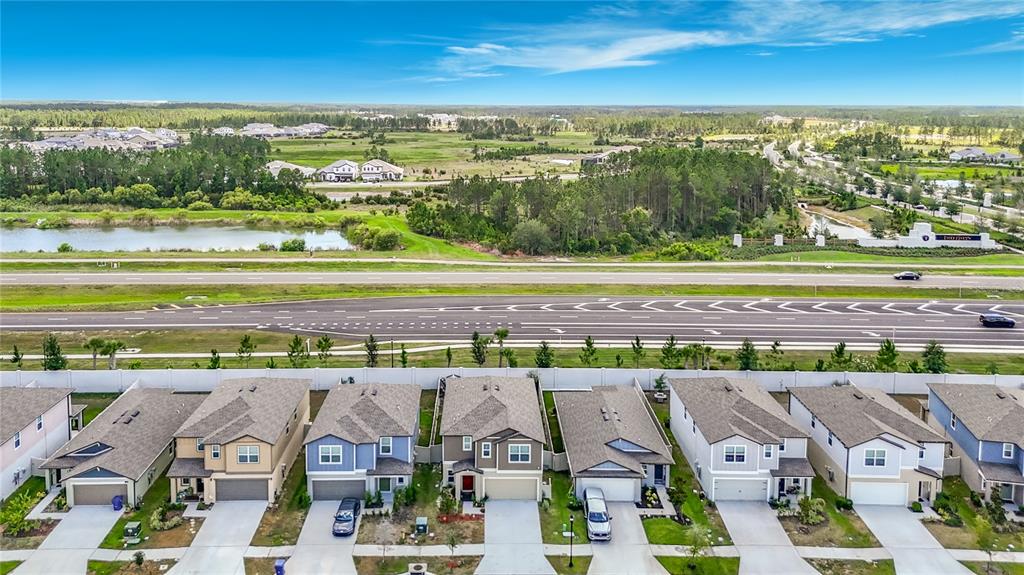 An aerial view shows a row of suburban houses facing a multi-lane highway and landscape — 35186 ACKLEY TRACE, ZEPHYRHILLS, FL