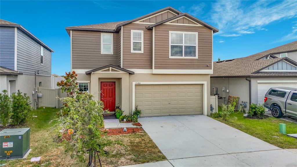 A two-story house with a red front door, a garage, and a concrete driveway — 35186 ACKLEY TRACE, ZEPHYRHILLS, FL