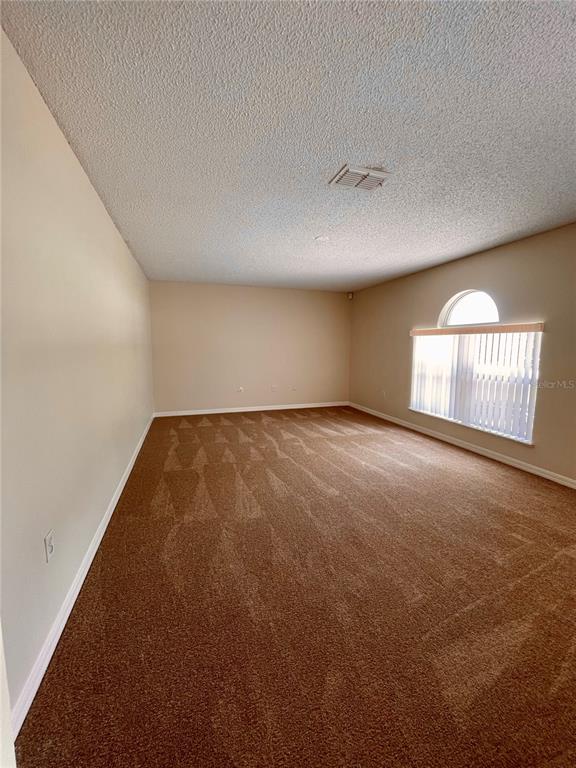 An empty room features tan walls, brown carpet, and an arched window with vertical blinds — 1304 DOVER DRIVE, KISSIMMEE, FL