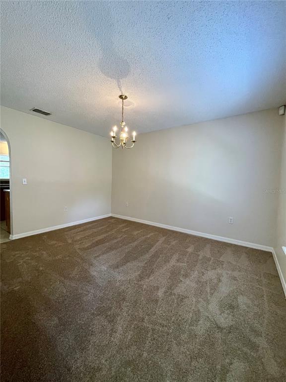 An empty dining room features beige walls, brown carpeting, and a traditional chandelier — 1304 DOVER DRIVE, KISSIMMEE, FL