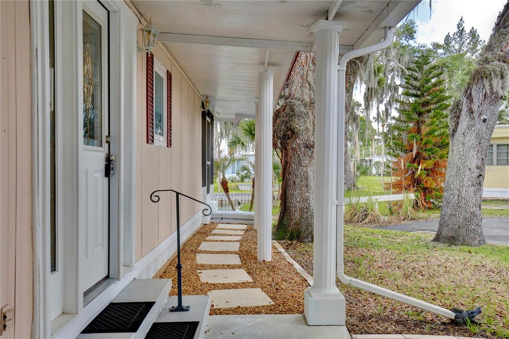 A covered porch with white columns, a stone walkway, and a front door with a lockbox — 105 CANAL VIEW, EUSTIS, FL