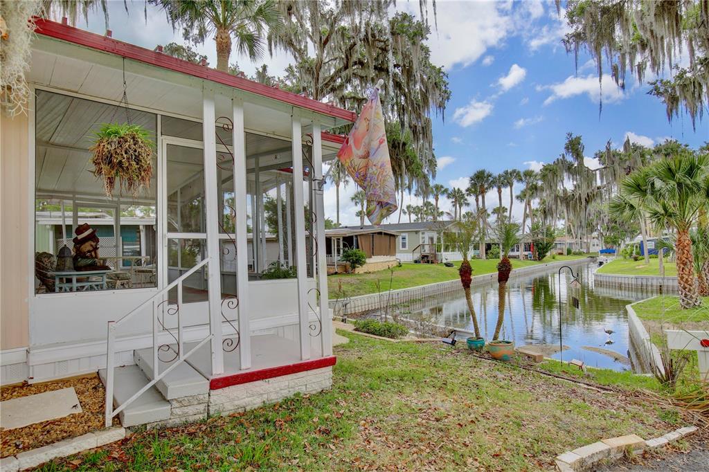 A screened-in porch overlooks a narrow canal lined with palm trees and Spanish moss — 105 CANAL VIEW, EUSTIS, FL