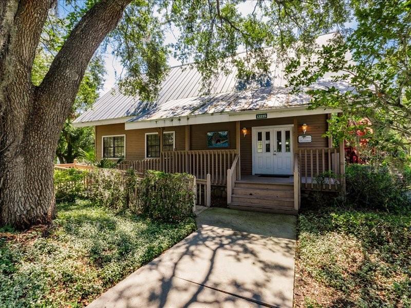 A wooden house with a metal roof and a front porch sits behind a large tree — 13075 SR-64 E, BRADENTON, FL