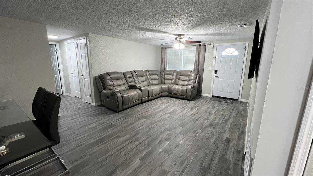 A living room features gray wood-look flooring, a large sectional sofa, and a ceiling fan — 2705 GARDNER PLACE, HOLIDAY, FL