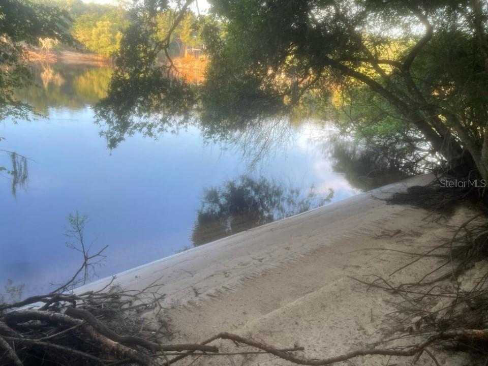 A sandy shoreline slopes down to a calm river under the shade of overhanging trees — 1263 NW 82ND TERRACE, BELL, FL
