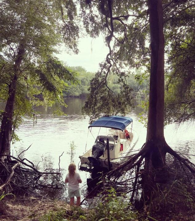A child stands on a wooded riverbank next to a small motorboat with a canopy — 1263 NW 82ND TERRACE, BELL, FL