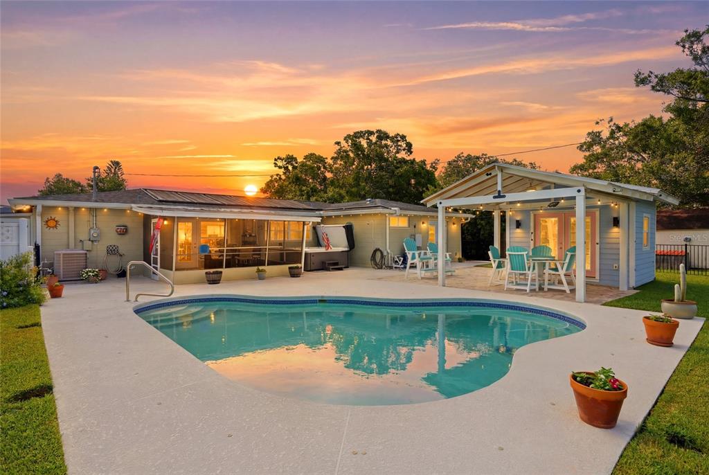 A backyard features a swimming pool, a covered patio, and a detached structure at sunset — 4822 60TH WAY N, KENNETH CITY, FL