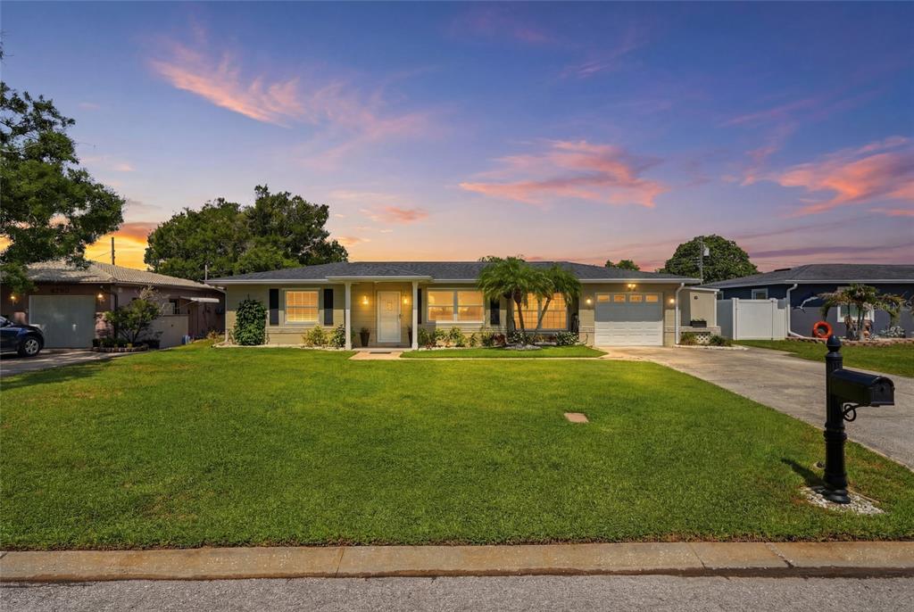 A single-story house with a green lawn, a driveway, and a palm tree at sunset — 4822 60TH WAY N, KENNETH CITY, FL