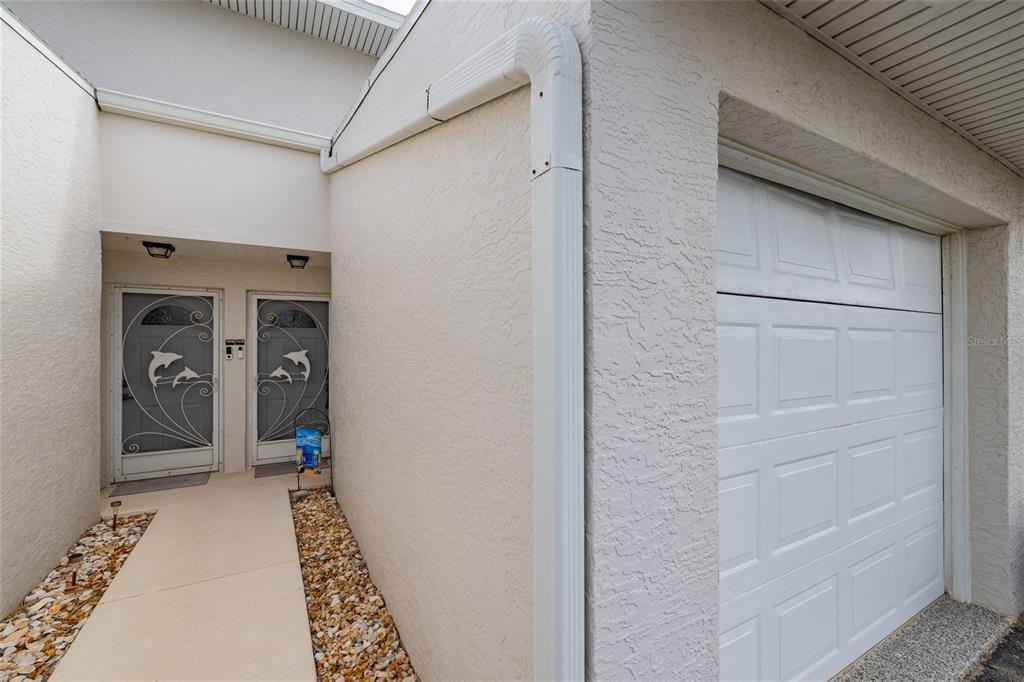 A concrete walkway leads to two front doors with dolphin-themed screen doors beside a garage — 2470 OCEAN SHORE BOULEVARD UNIT 105, ORMOND BEACH, FL