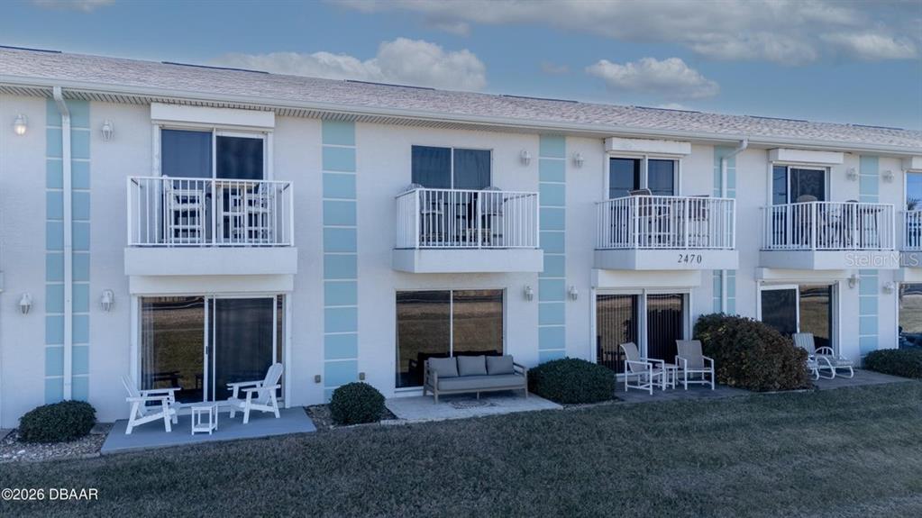 A two-story building exterior with white walls, blue accents, balconies, and ground-level patios — 2470 OCEAN SHORE BOULEVARD UNIT 105, ORMOND BEACH, FL