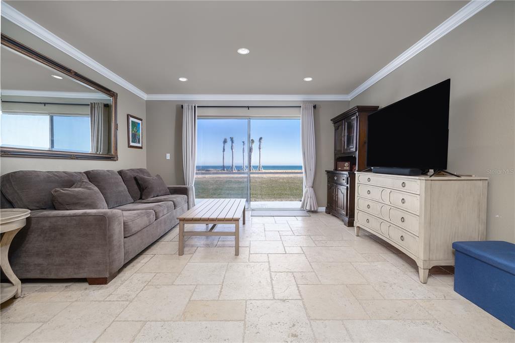 A living room features tile flooring, a gray sofa, a television, and sliding glass doors — 2470 OCEAN SHORE BOULEVARD UNIT 105, ORMOND BEACH, FL