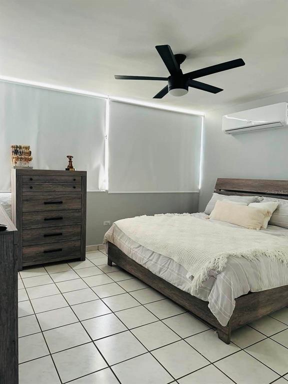 A bedroom features a wooden bed frame, a matching dresser, white tile floors, and a ceiling fan — Calle 10 S7, TOA ALTA, PR