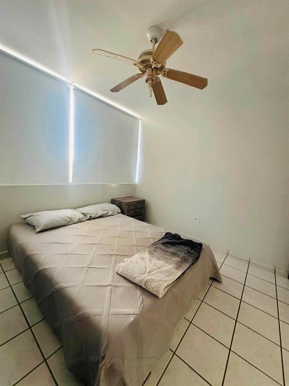 A bedroom features a bed with a patterned blanket, a ceiling fan, and tiled floors — Calle 10 S7, TOA ALTA, PR