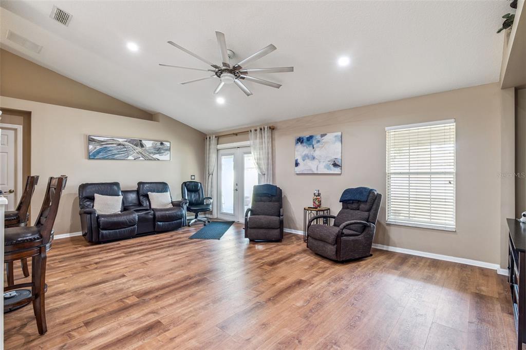 A living room with wood-look flooring, a ceiling fan, leather seating, and glass patio doors — 1545 OVERTON STREET, DELTONA, FL