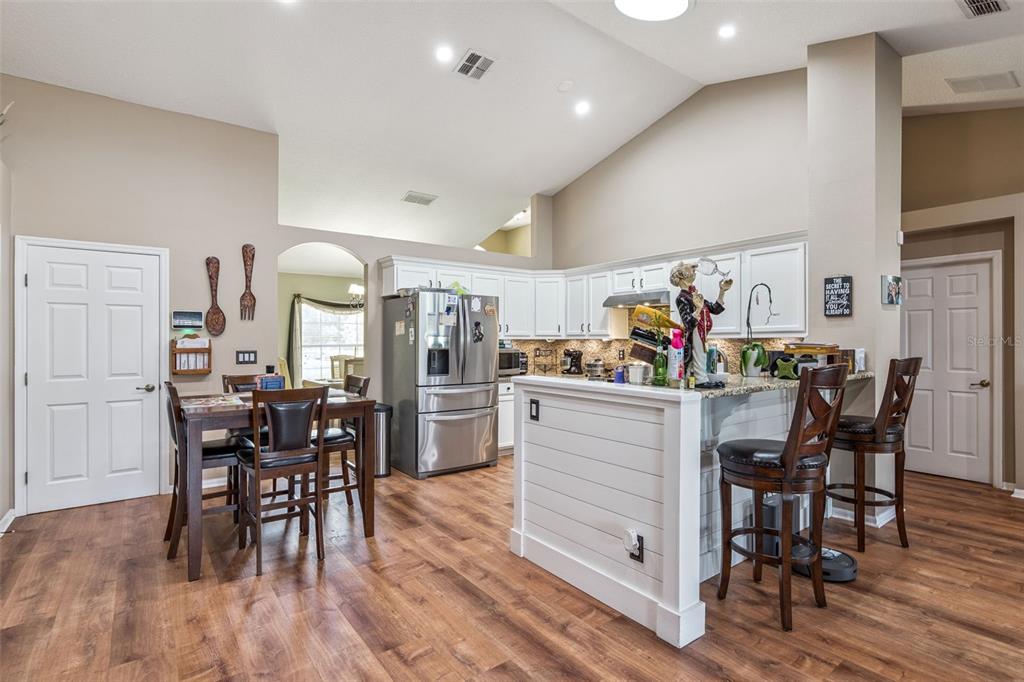 A kitchen with white cabinets, stainless steel appliances, a breakfast bar, and wood-look flooring — 1545 OVERTON STREET, DELTONA, FL