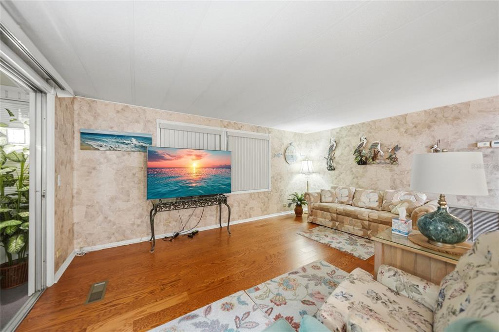 A living room with wood flooring, patterned wallpaper, a television on a stand, and furniture — 3450 GRAPEFRUIT LANE, ESTERO, FL