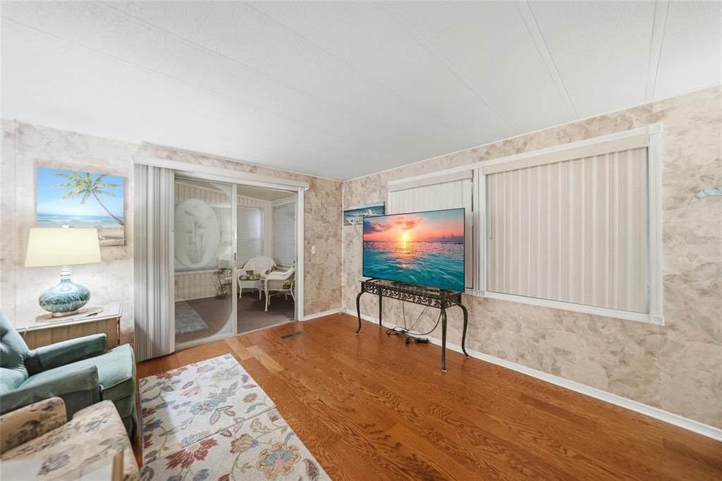 A living room features hardwood floors, textured wallpaper, a television on a stand, and sliding doors — 3450 GRAPEFRUIT LANE, ESTERO, FL