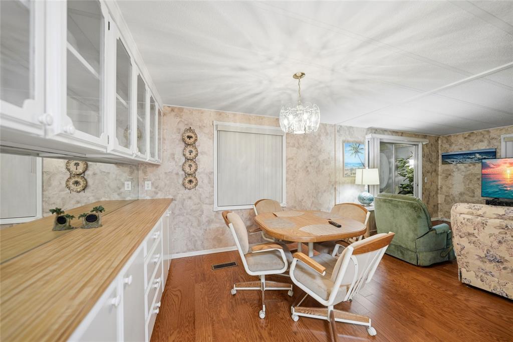 A dining area features a wooden table, rolling chairs, white cabinetry, and patterned wallpaper — 3450 GRAPEFRUIT LANE, ESTERO, FL