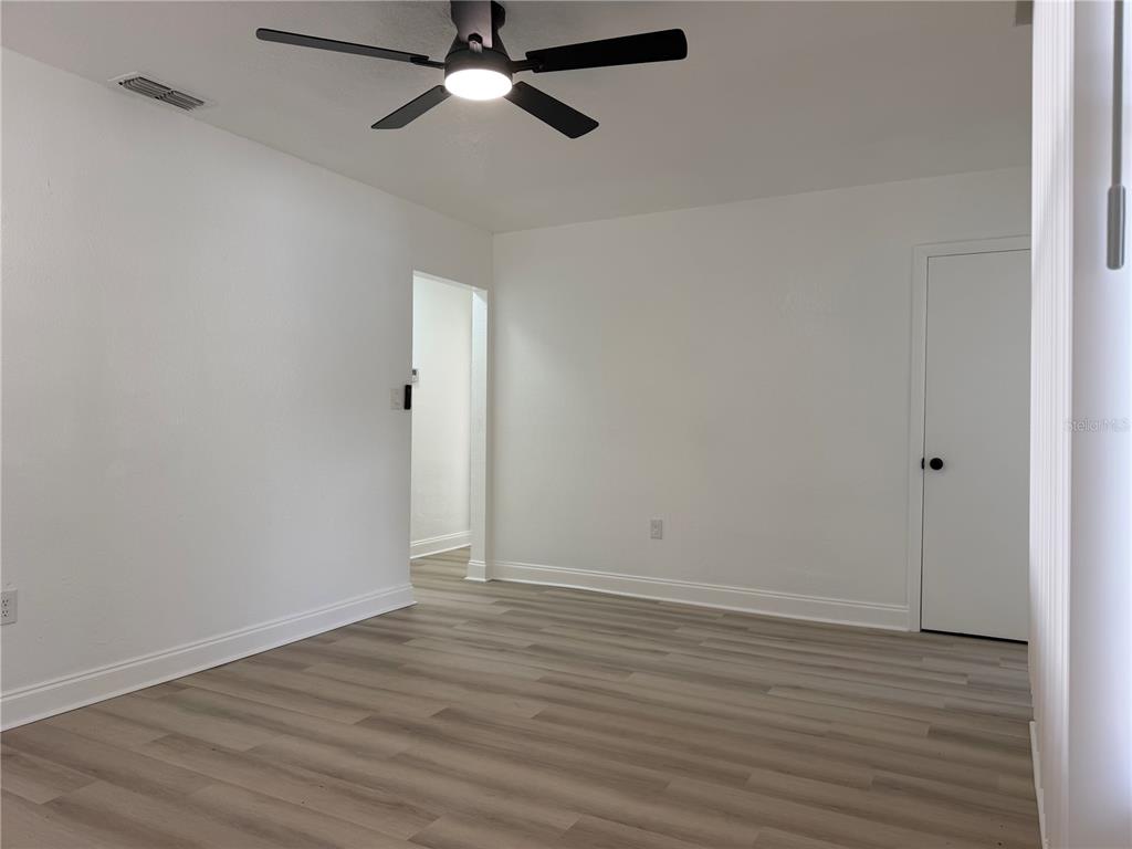 An empty room features white walls, light wood-look flooring, a ceiling fan, and a doorway — 1705 E BIRD STREET, TAMPA, FL