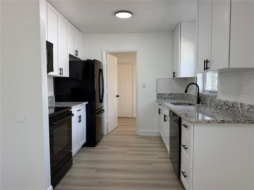 A kitchen features white cabinets, black appliances, granite countertops, and light wood-look flooring — 1705 E BIRD STREET, TAMPA, FL