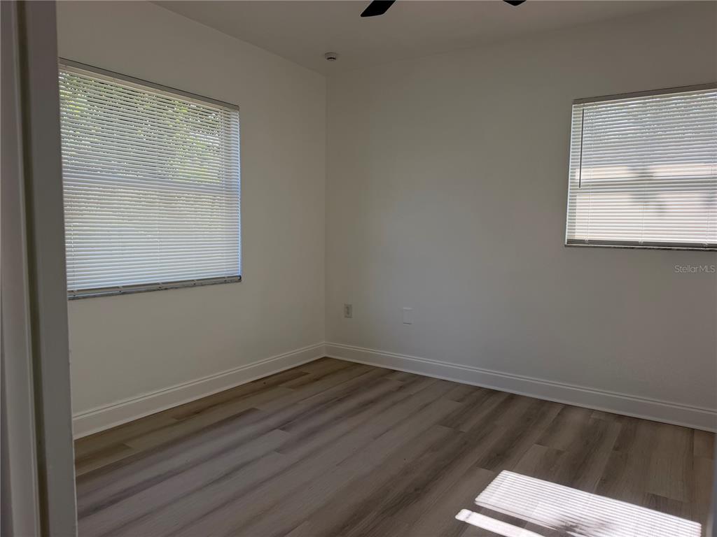 An empty bedroom features white walls, light wood-look flooring, and two windows with blinds — 1705 E BIRD STREET, TAMPA, FL