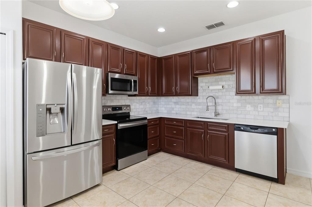 A kitchen with dark wood cabinets, stainless steel appliances, white countertops, and a subway tile backsplash — 2628 BALFORN TOWER WAY, WINTER GARDEN, FL