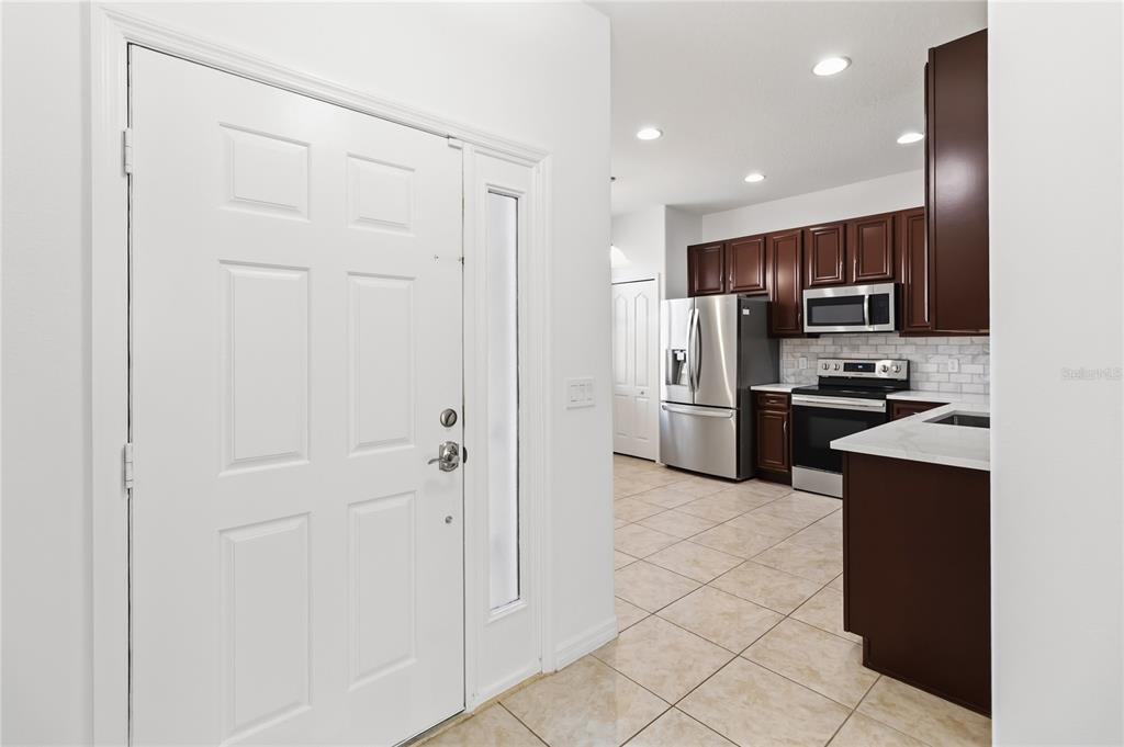 A white front door opens into a kitchen with dark wood cabinets and tile flooring — 2628 BALFORN TOWER WAY, WINTER GARDEN, FL