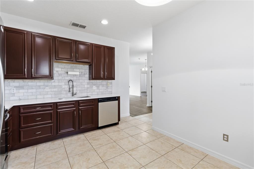 A kitchen features dark wood cabinets, white countertops, a subway tile backsplash, and tile flooring — 2628 BALFORN TOWER WAY, WINTER GARDEN, FL