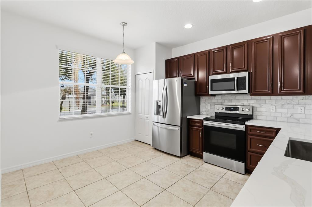 A kitchen with dark wood cabinets, stainless steel appliances, and a dining area with tile flooring — 2628 BALFORN TOWER WAY, WINTER GARDEN, FL