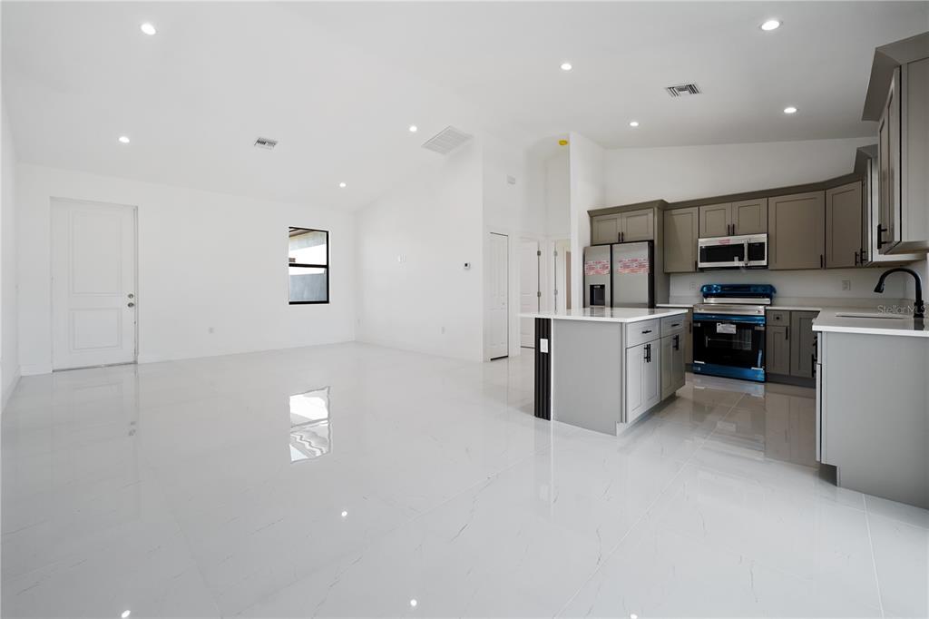 A bright, open-concept kitchen and living area featuring white tile floors and grey cabinetry — 2458 NW 9TH TERRACE, CAPE CORAL, FL