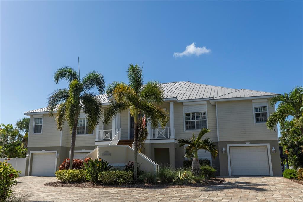 A two-story house with a metal roof, elevated entrance, and palm trees in the front yard — 100 BUCCANEER BEND, PLACIDA, FL