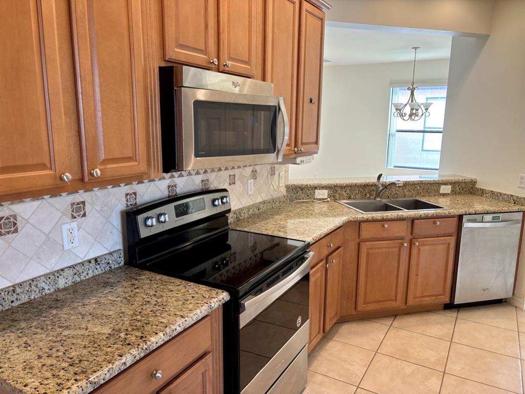 A kitchen features wood cabinets, granite countertops, stainless steel appliances, and a tiled backsplash — 229 SHELL FALLS DRIVE, APOLLO BEACH, FL