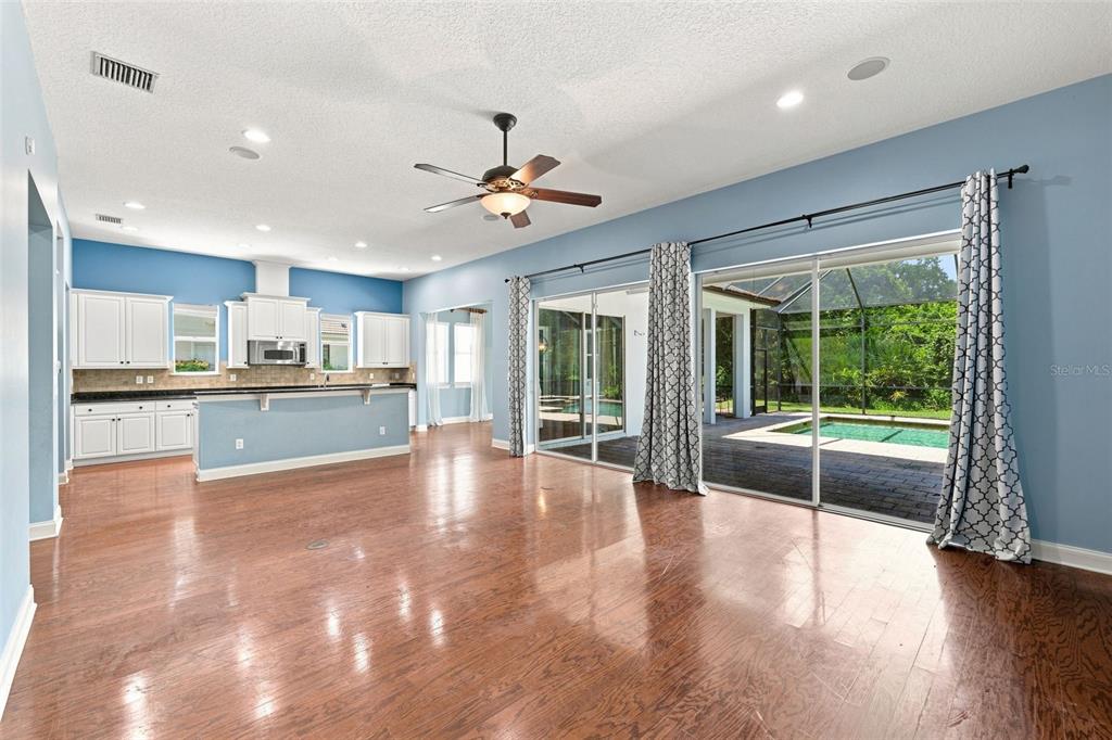 A spacious living area with hardwood floors, a kitchen, and sliding doors opening to a pool — 21201 SKY VISTA DRIVE, LAND O LAKES, FL