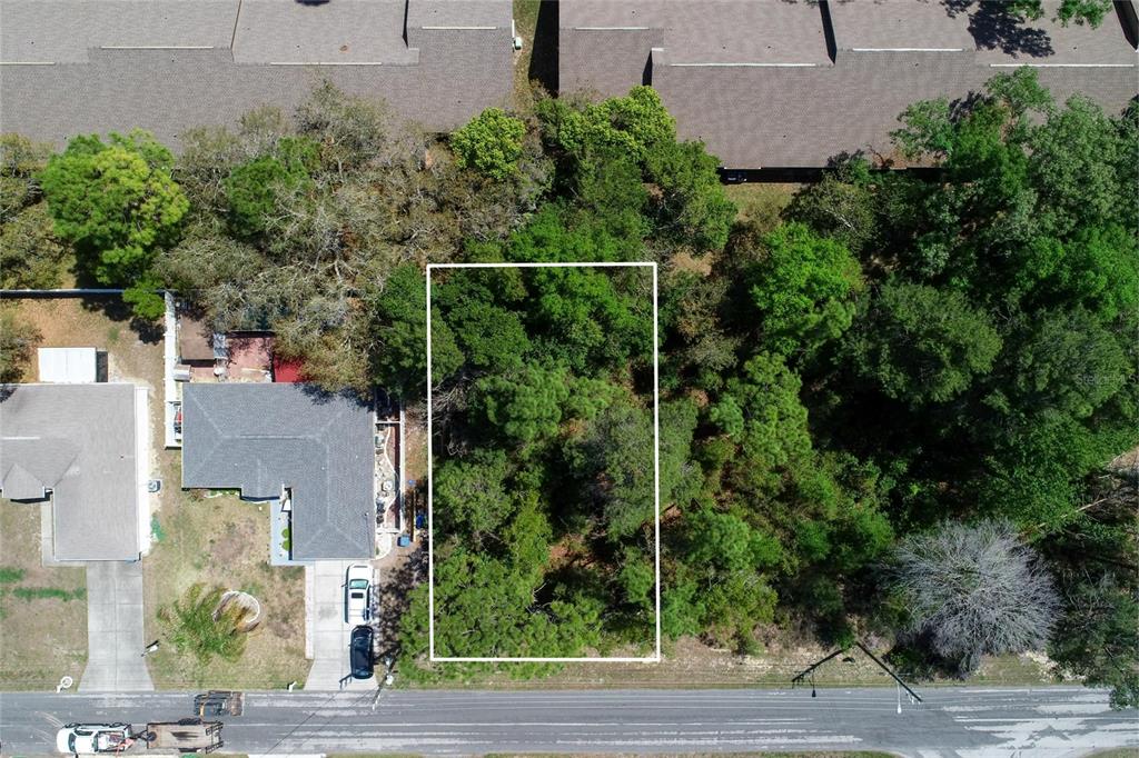 An aerial view shows a rectangular, wooded vacant lot situated between a house and trees — TOMAHAWK AVENUE, SPRING HILL, FL