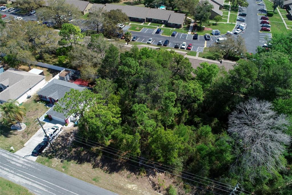 An aerial view shows a wooded lot situated between a residential house and a parking lot — TOMAHAWK AVENUE, SPRING HILL, FL
