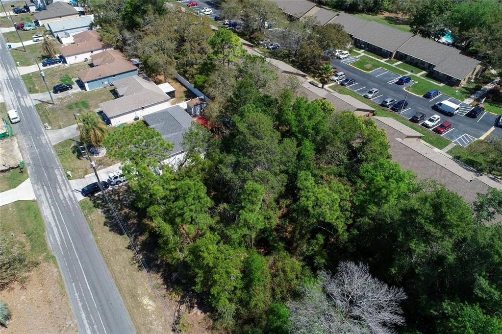An aerial view shows a wooded vacant lot situated between a residential street and a parking lot — TOMAHAWK AVENUE, SPRING HILL, FL