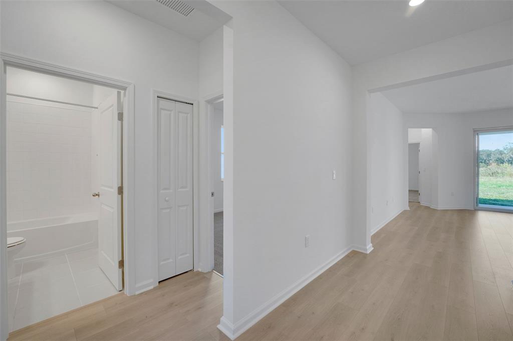 A hallway with light wood flooring leads to a bathroom, a closet, and living space — 300 MEREDITH BOULEVARD, WINTER HAVEN, FL