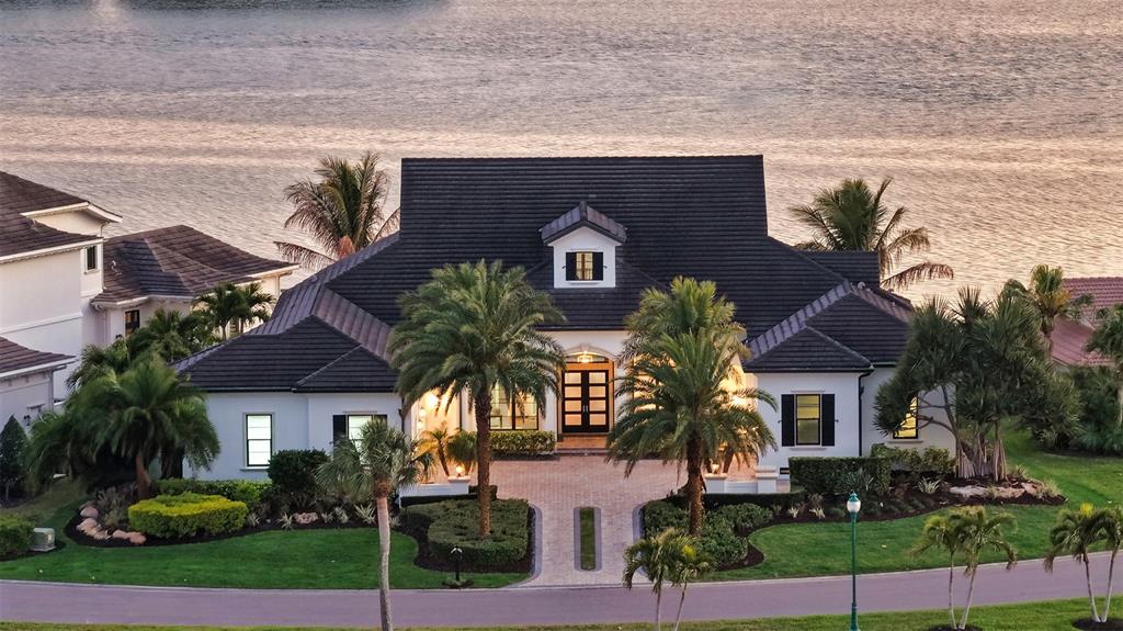 A white house with a dark roof and palm trees sits along a waterfront — 313 LOOKOUT POINT DRIVE, OSPREY, FL