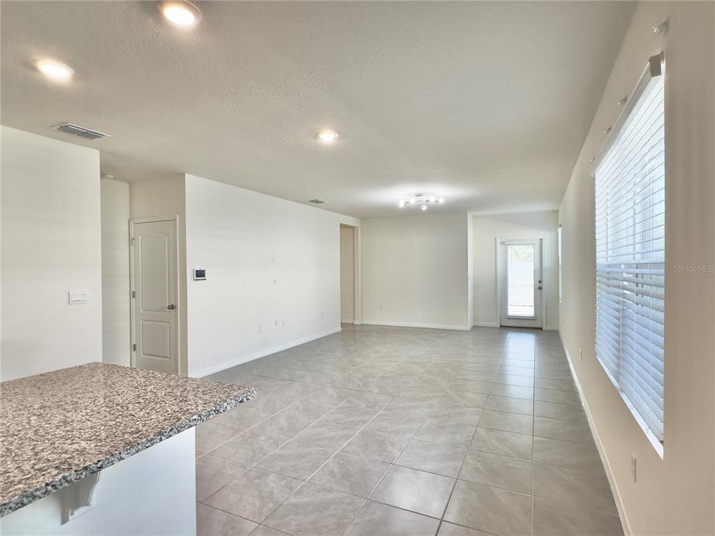 An open-concept living and dining area features a blue sectional sofa, tile floors, and kitchen — 2606 ANGEL FALLS DRIVE, DAVENPORT, FL