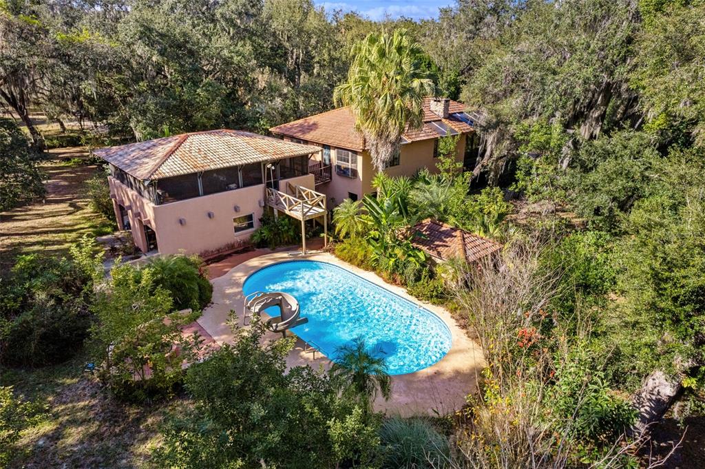 An aerial view shows a two-story house with a pool, slide, and surrounding wooded landscape — 27910 DEBBIE ROAD, OKAHUMPKA, FL